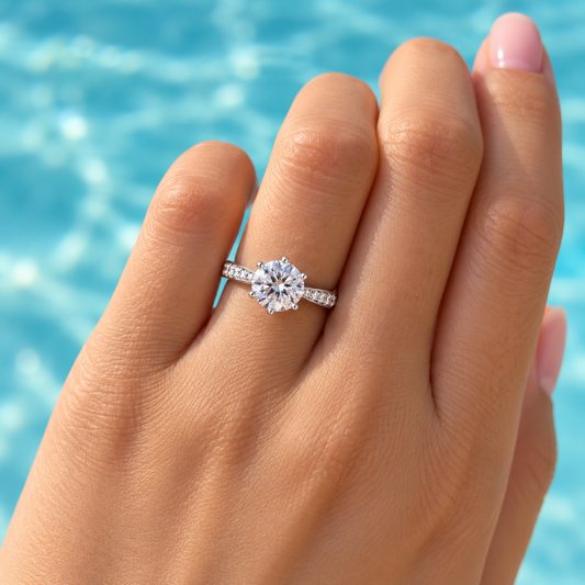 NEARHELD six-prong moissanite ring worn on a hand against a blue water background