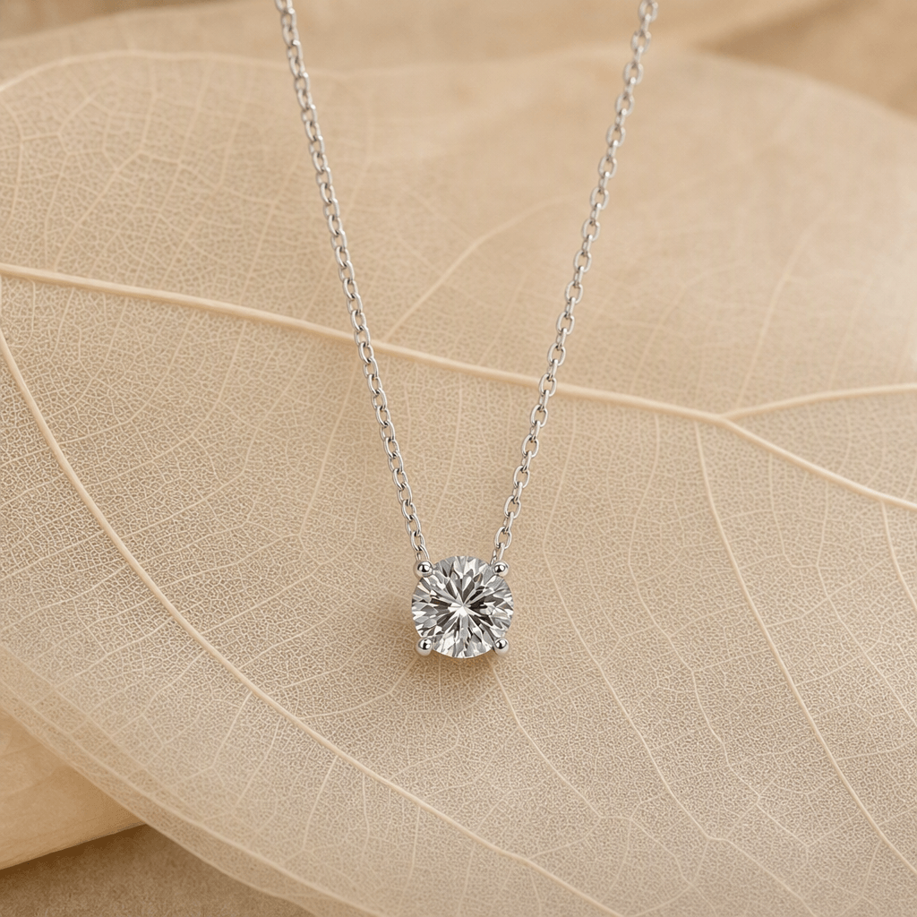 Silver four-prong moissanite pendant necklace styled on warm leaves