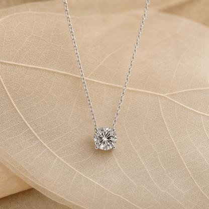 Silver four-prong moissanite pendant necklace styled on warm leaves