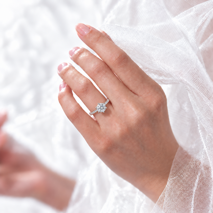 Six-prong round moissanite ring worn on a hand beside soft white tulle.