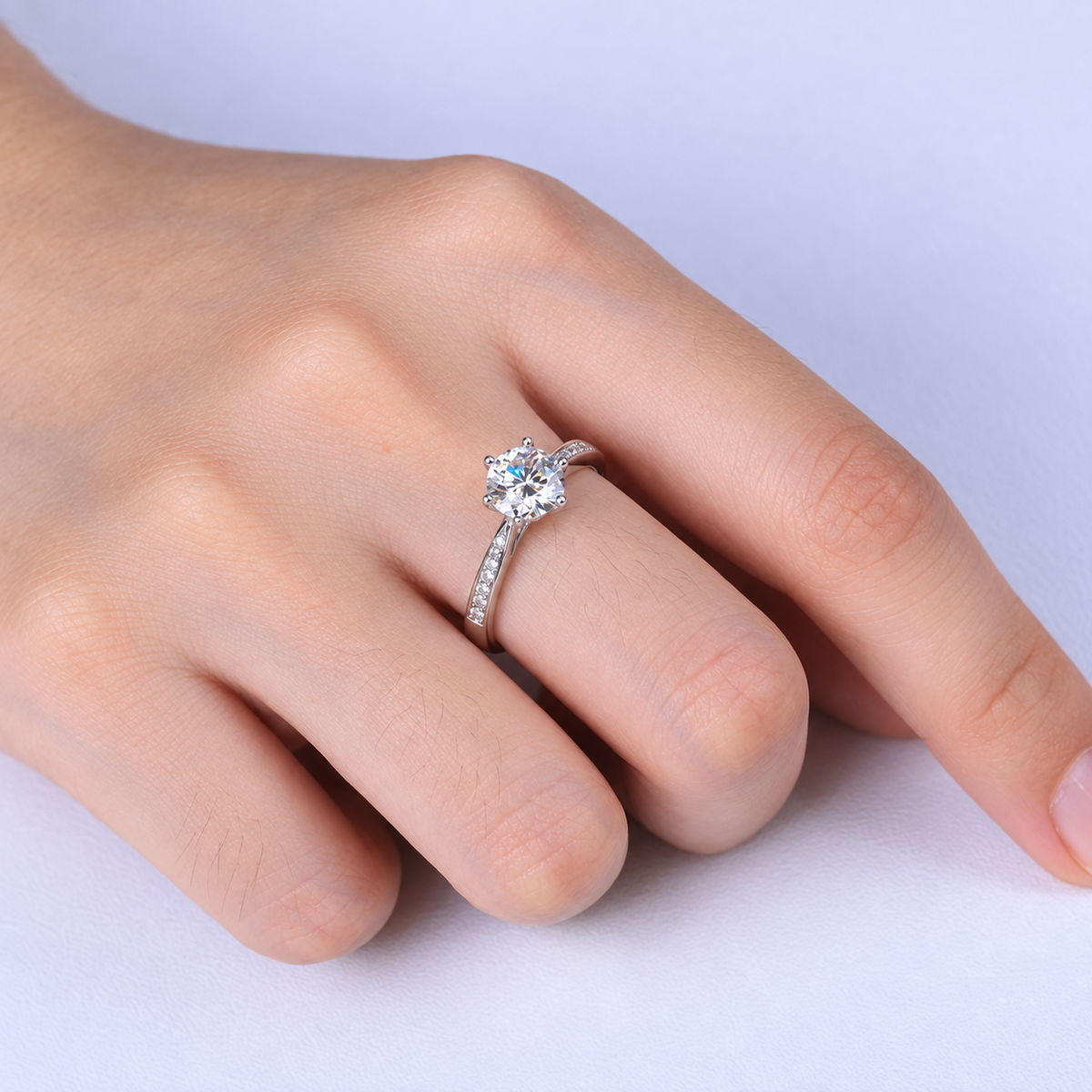 Close-up of the round moissanite ring with pavé shoulders worn on a hand.