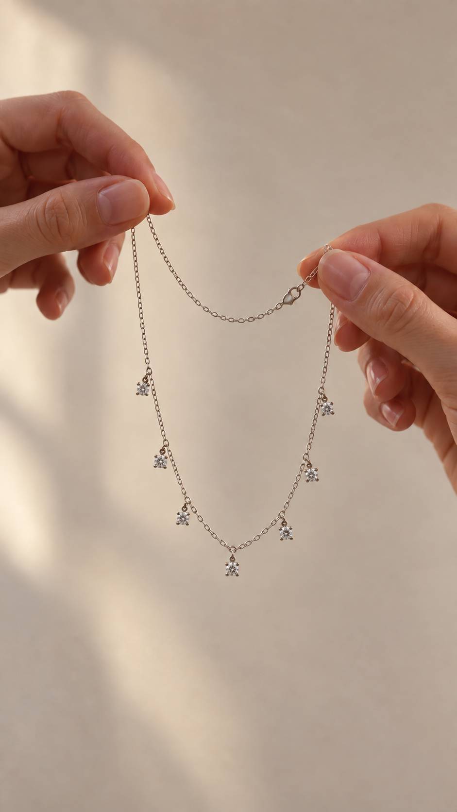 Seven-stone moissanite sterling silver necklace suspended between two hands in warm natural light