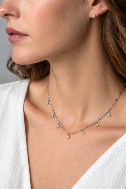 Seven-stone moissanite sterling silver necklace worn with a white V-neck shirt